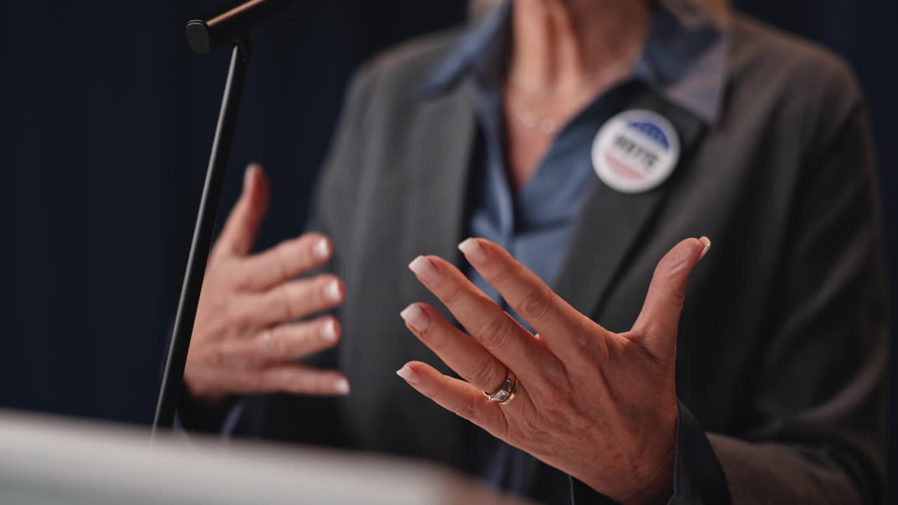 A woman gives a speech at a podium with a vote button on her lapel