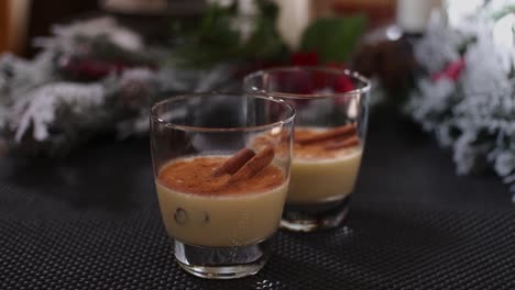 Un-Empujón-Lento-En-Dos-Vasos-De-Bebida-Navideña-Ponche-De-Huevo-Navideño-Adornado-Con-Palitos-De-Canela