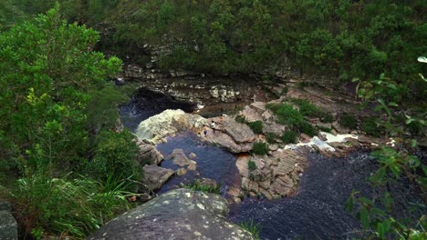 Tilting-down-4K-shot-revealing-the-Devil's-Pit-from-the-trail-above-in-the-Chapada-Diamantina-National-Park-in-Northeastern-Brazil-on-a-rainy-overcast-day-with-people-below-near-the-water