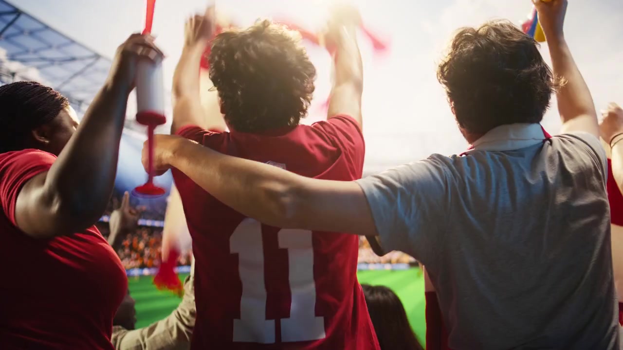 Primer plano de personas viendo un partido de fútbol intenso, entonando cánticos a viva voz