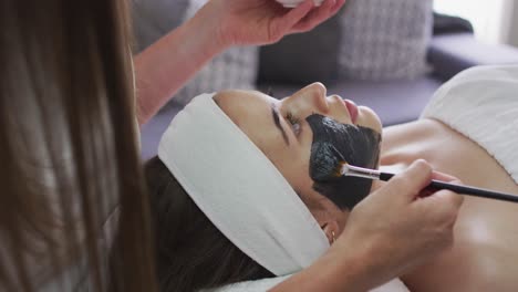 caucasian woman lying back while beautician gives her a face mask