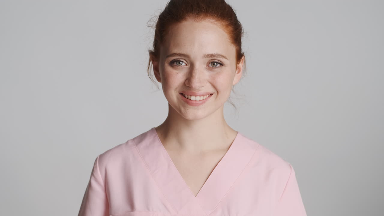 enfermera pelirroja frente a la cámara sobre un fondo gris.