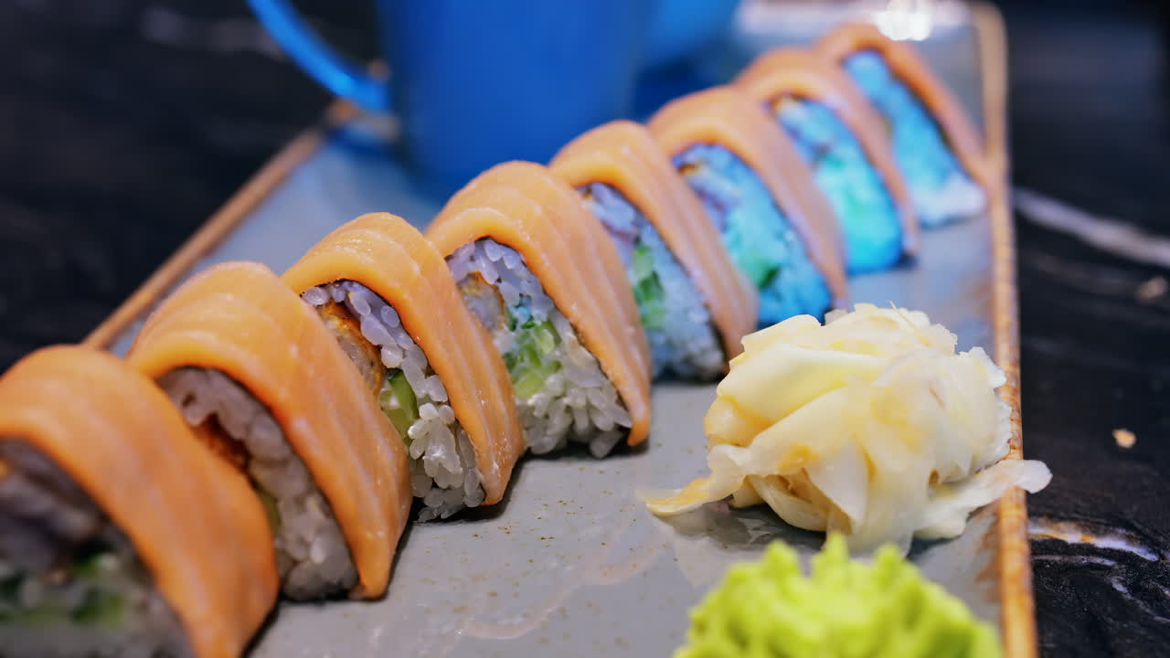 Close up of triangle shaped salmon sushi on a platter with wasabi and gari