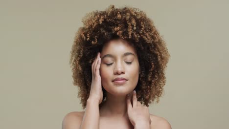 biracial woman with dark hair touching face on beige background with copy space, slow motion