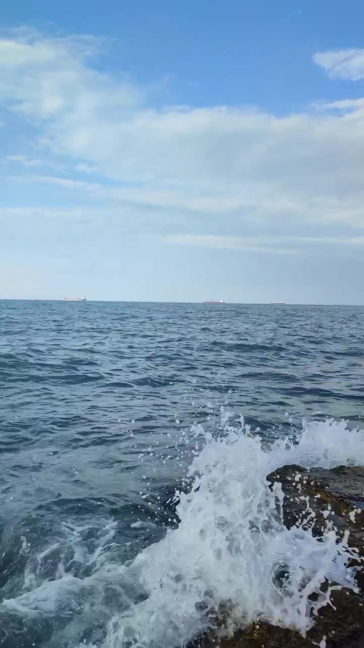 Kayalık kıyıya çarpan dalgalar, bulutlu gökyüzünün altında uzak ufka doğru uzanan sakin denizle. Gündüz vakti İskoçya, Birleşik Krallık'ta huzurlu kıyı manzarası