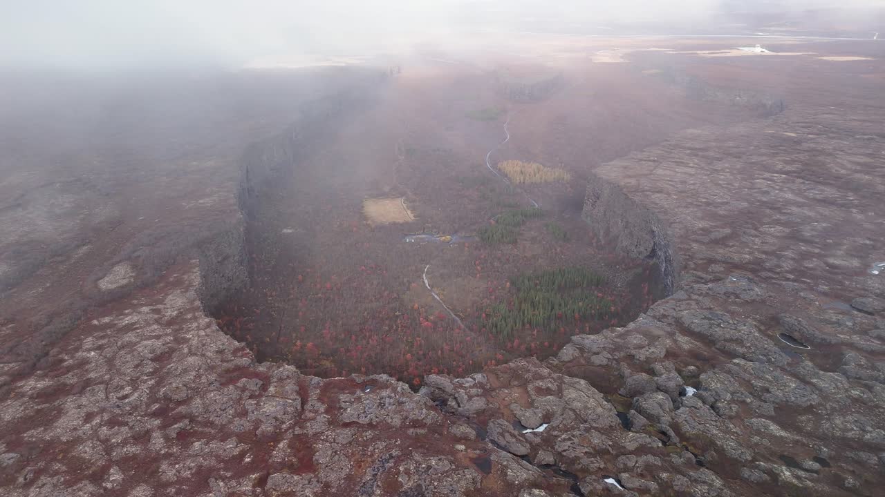 Aerial flight over Asbyrgi glacier ravine during foggy day in Iceland. Autumn season with colorful plants and trees in the valley.