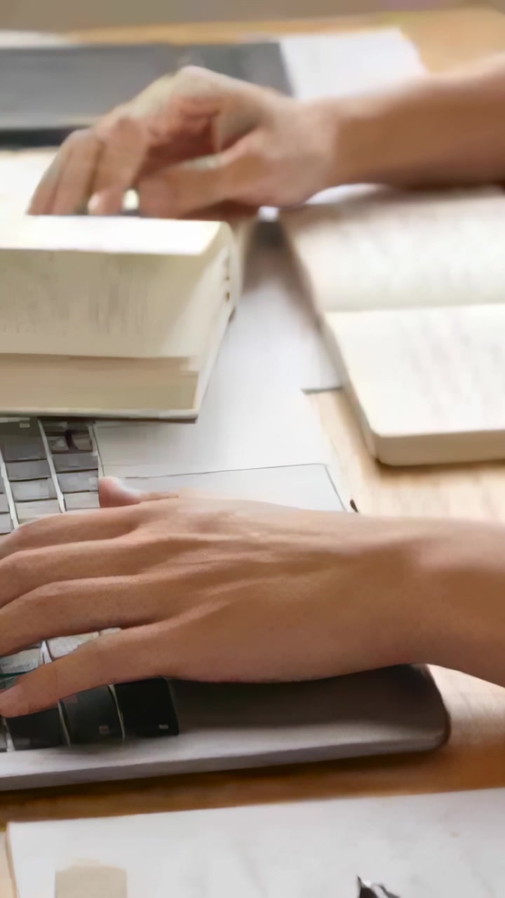 Vertikal video: Studiehender begynner å vekselvis skrive på laptop og bla i bøker ved pulten med penn