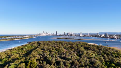 drone footage captures gold coast's lush greenery and vibrant skyline under clear blue skies, showcasing natural beauty and urban landscape