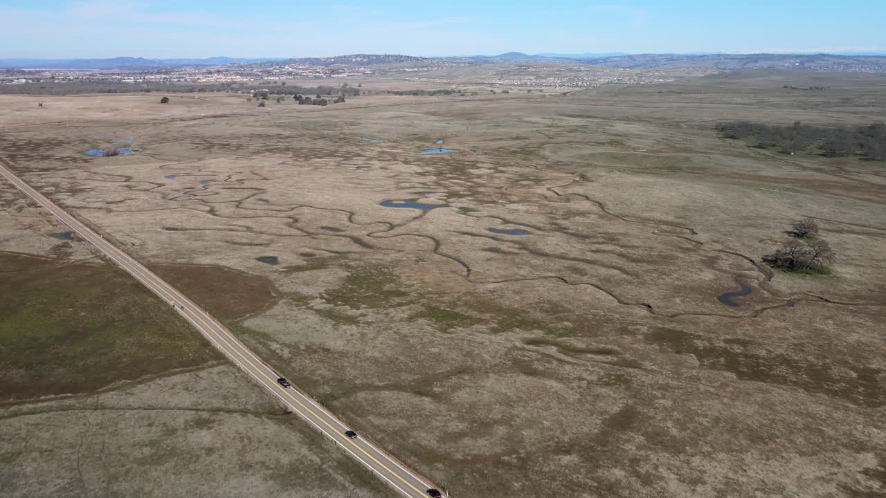 una carretera con automóviles atraviesa un campo cubierto de estanques primaverales protegidos en el valle central de california visto en un episodio de california's gold
