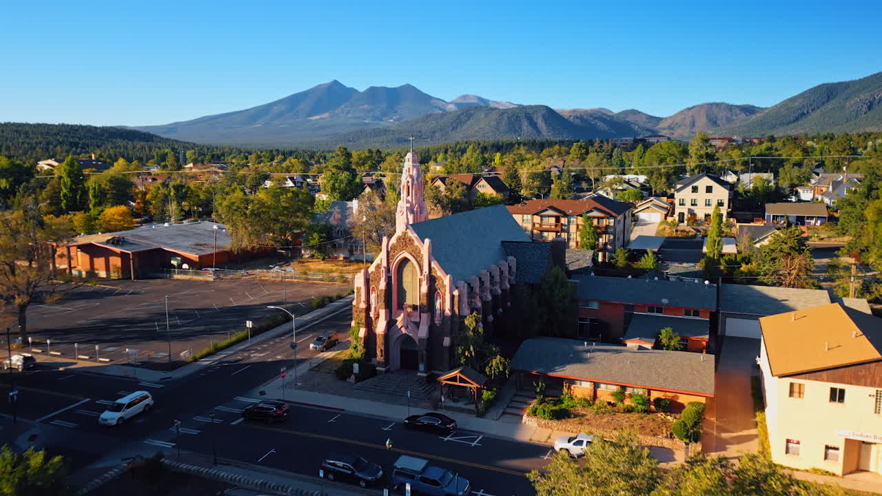 Approaching a beautiful church in Flagstaff, Arizona, USA. Amazing scenery of green cityscape and sunlit verdant mountains from drone