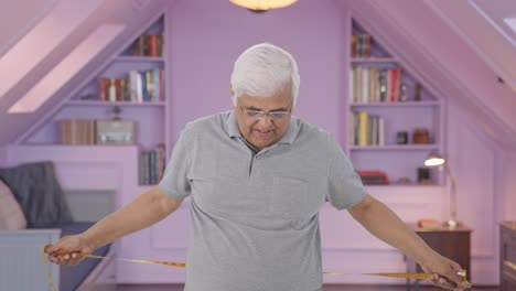 sad indian old man checking his waist size using inch tape