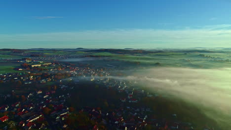 Una-Vista-Aérea-Sobre-Una-Niebla-Baja-Crea-Una-Vista-De-Ensueño-De-Un-Pueblo-Y-Sus-Prados.