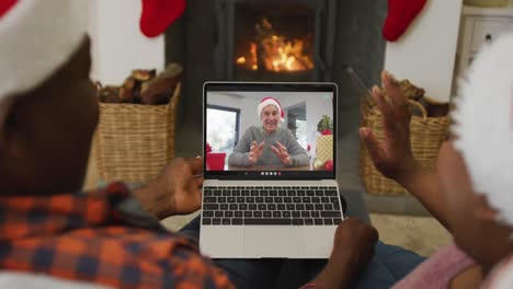 pareja afroamericana con sombreros de santa usando una computadora portátil para una videollamada de navidad con un hombre en la pantalla