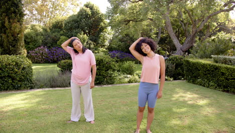 exercising in garden, mother and adult daughter stretching necks and smiling outdoors