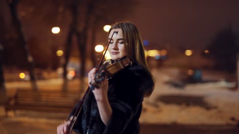 Young girl playing violin outdoors. Professional violinist woman with the violin at late evening