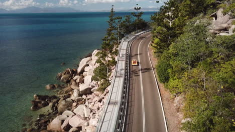 Luftaufnahme-Des-Klassischen-Strandbuggys-Mit-Offenem-Verdeck,-Der-Entlang-Der-Klippenküstenstraße-Neben-Kristallklarem-Tropischem-Wasser-Und-üppigem-Grünen-Wald-Fährt