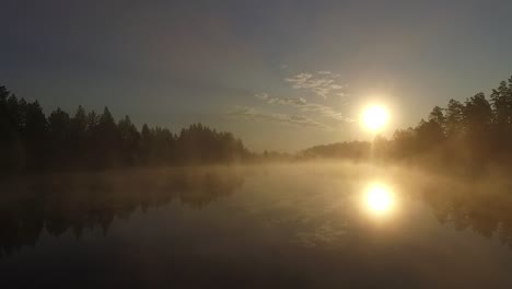 Misty-morning-sunlight-over-autumn-forest-lake-and-scenic-countryside-landscape-aerial-wide-view