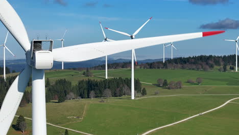 wind turbines spin on a green hillside under a clear blue sky, captured in a close-up fly-by shot