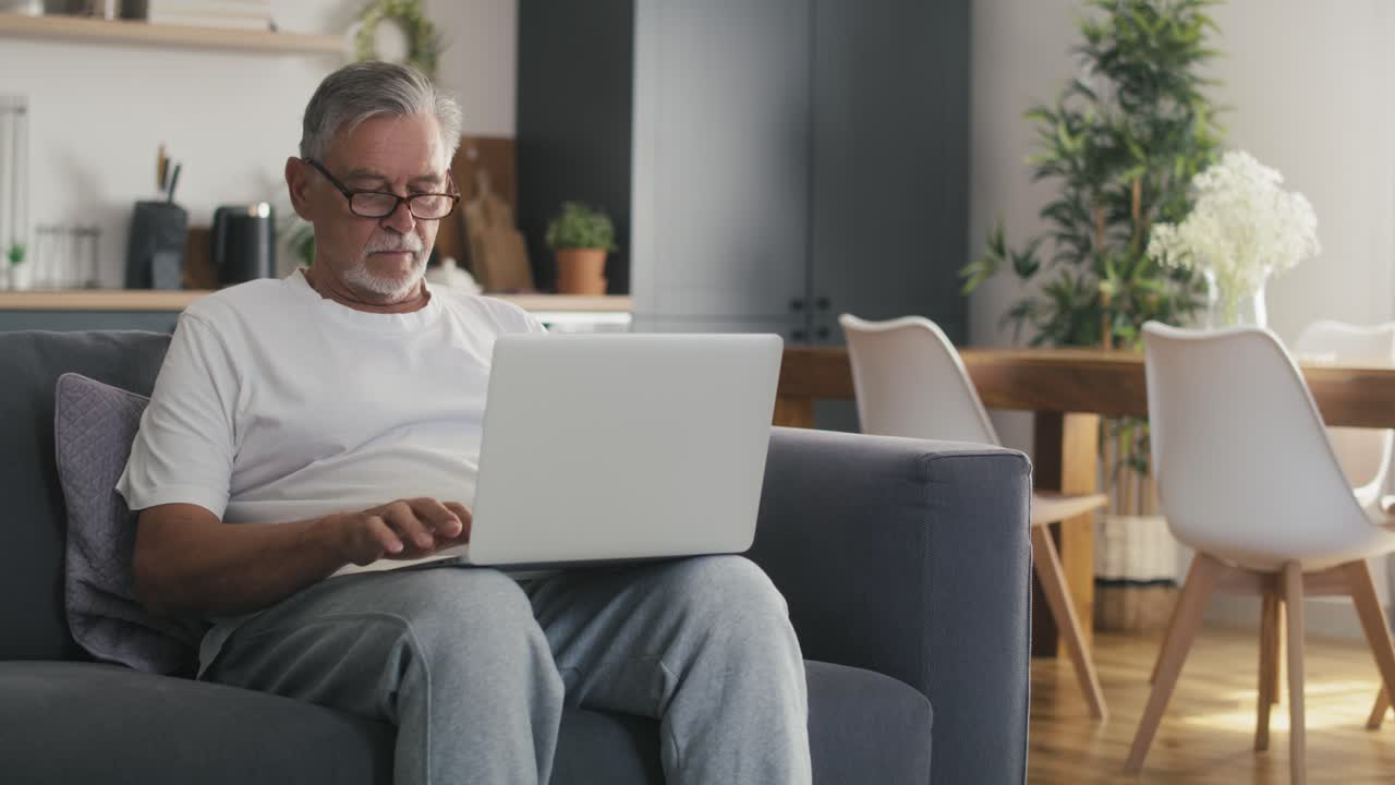Senior caucasian man sitting at couch and using laptop.