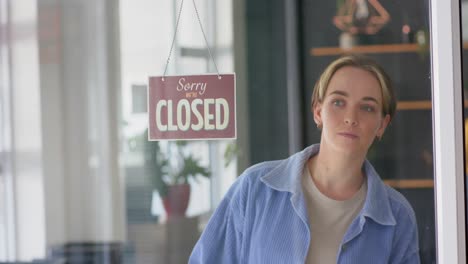 smiling caucasian female hairdresser turning shop sign to open on door of hair salon, in slow motion