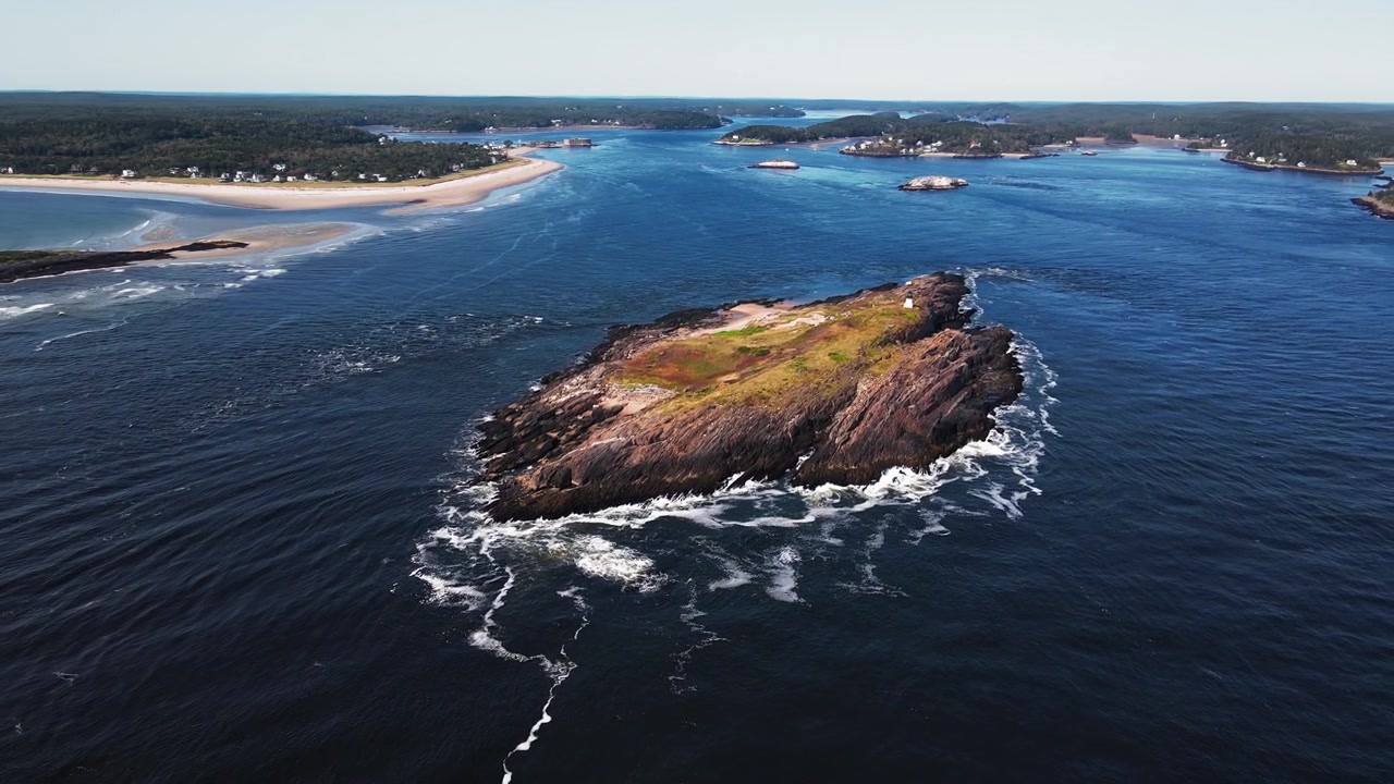 Ampia veduta aerea che rivela lo storico faro di Pond Island su una piccola isola vicino a Popham Beach, Maine, con gabbiani in volo e onde che si infrangono sull'isola rocciosa alla foce del fiume Kennebec