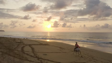 Fairytale-scenery-with-female-in-dress-riding-horse-on-beach-at-sunrise