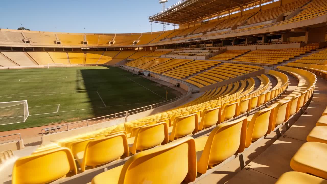 Eine Kamerafahrt bewegt sich entlang gelber Sitze im Stadion und enthüllt den grünen Rasen und das Tor, mit Platz für Text.
