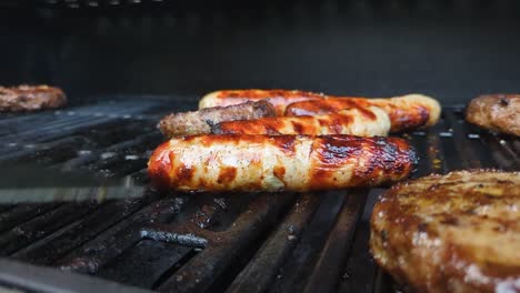 hamburguesas de carne y salchichas largas siendo volteadas en la barbacoa en verano