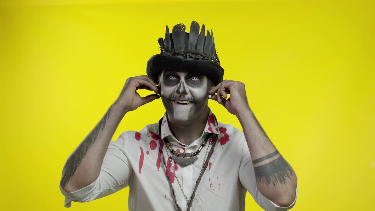 un hombre siniestro con un horrible maquillaje de halloween se pone auriculares, comienza a bailar, a celebrar