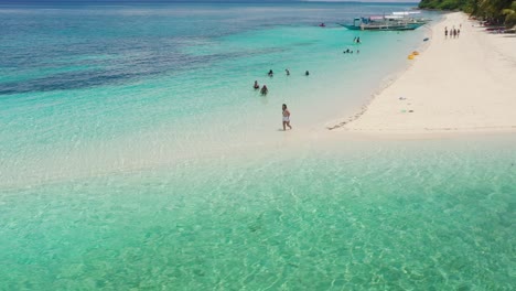 tourists on white sand tropical beach with tranquil turquoise ocean and blue sky - aerial drone shot