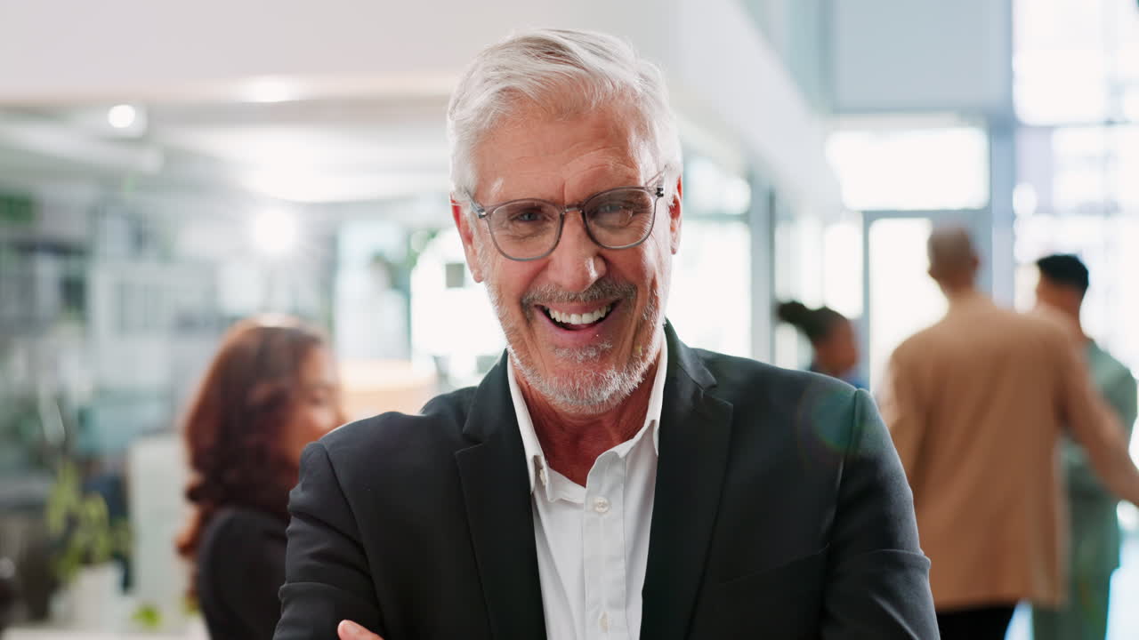 Smiling businessman in a suit and glasses stands in front of a group of colleagues.
