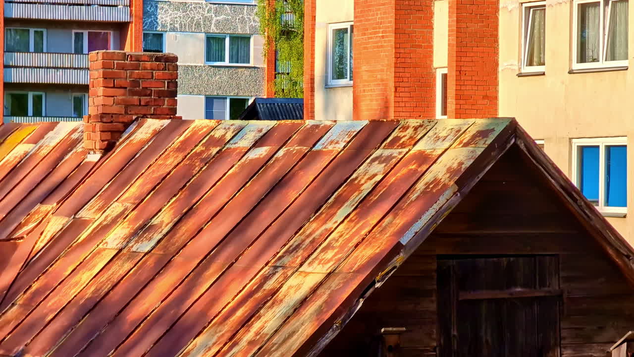 Rusted Tin Roof with Brick Chimney in Front of Urban Apartment Buildings at Sunset