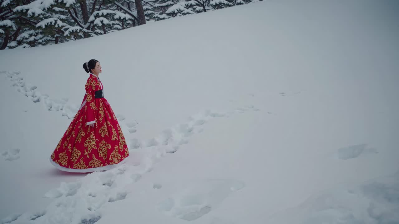 A woman in a red traditional dress walks through snow, leaving footprints
