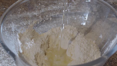 water being poured into a glass bowl of flour with a well in the centre