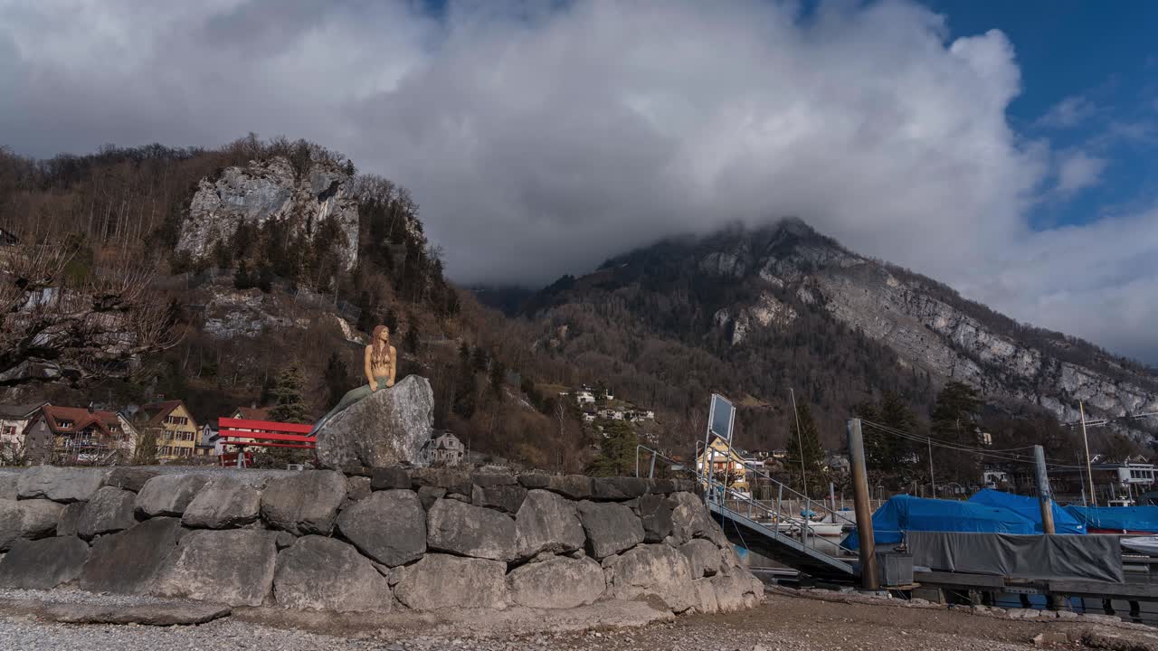 Alpy Szwajcarskie i góry w tle w pobliżu jeziora Walensee w Amden. Syrena na pierwszym planie przy pomoście i łodziach rybackich. Chmury kłębią się na szczycie