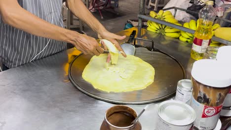 a street vendor in phuket, thailand, prepares banana roti on a hot griddle, showcasing traditional street food techniques