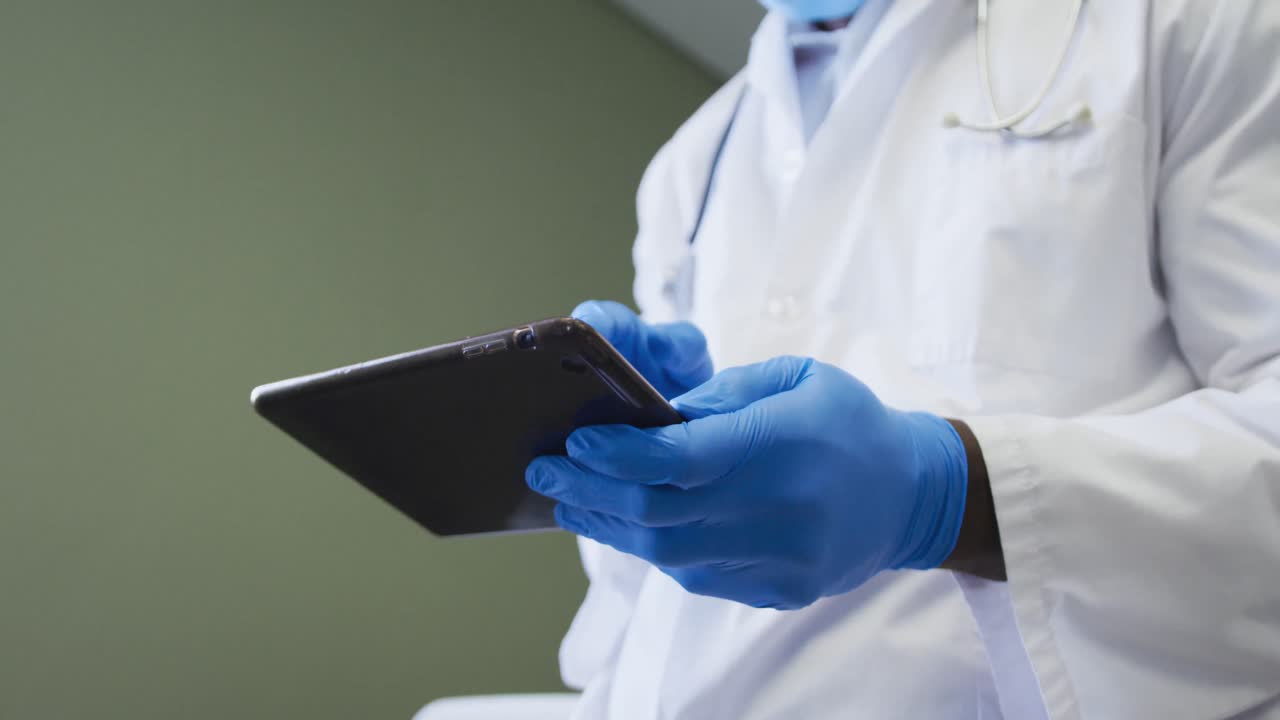 médico afroamericano de alto rango que usa una máscara facial usando una tableta digital en el hospital