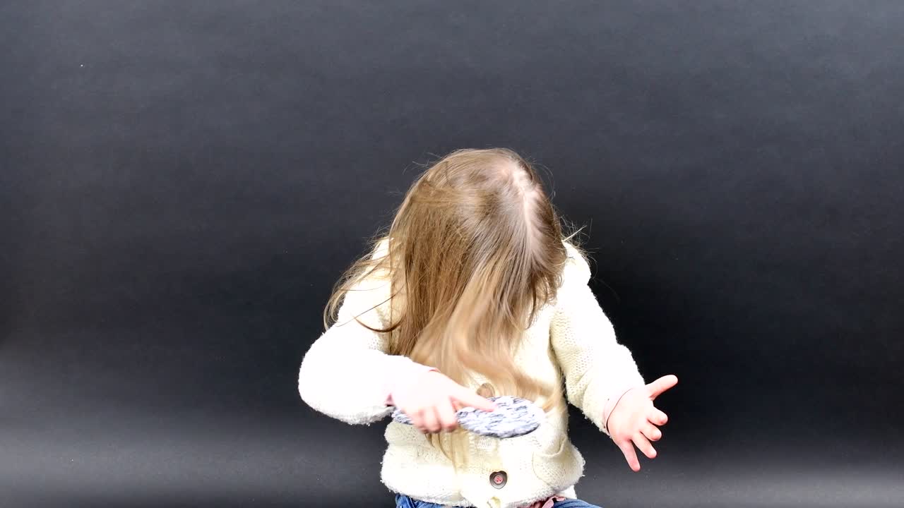 Cute girl combs her hair. Small girl is dressed in winter clothing. Cute little girl on black background.
