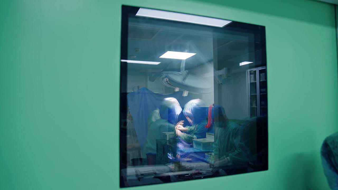 Reflection of surgeons working in the surgery room. Footage at the door with window.