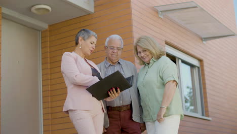 female agent holding folder with real estate documents, discussing details of sale with happy clients