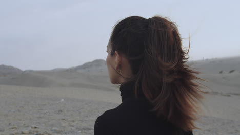 close-up of the back of a woman dressed in black walking through the desert in the morning while the wind blows and moves her hair