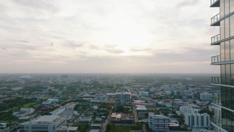 Fly-around-modern-high-rise-apartment-building-with-balconies.-Aerial-panoramic-view-of-urban-neighbourhood-against-sunset.-Miami,-USA