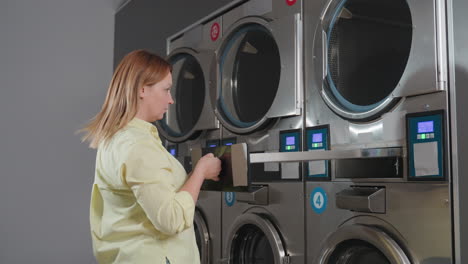 laundry worker pushes industrial washer filter drawer into compartment, locks with key after cleaning, performing routine maintenance in laundromat, professional service with safety procedure ensured
