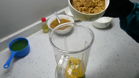 The chef is pouring ingredients into a container and blender for grinding purposes. These ingredients will be thoroughly blended and ready for the next steps.