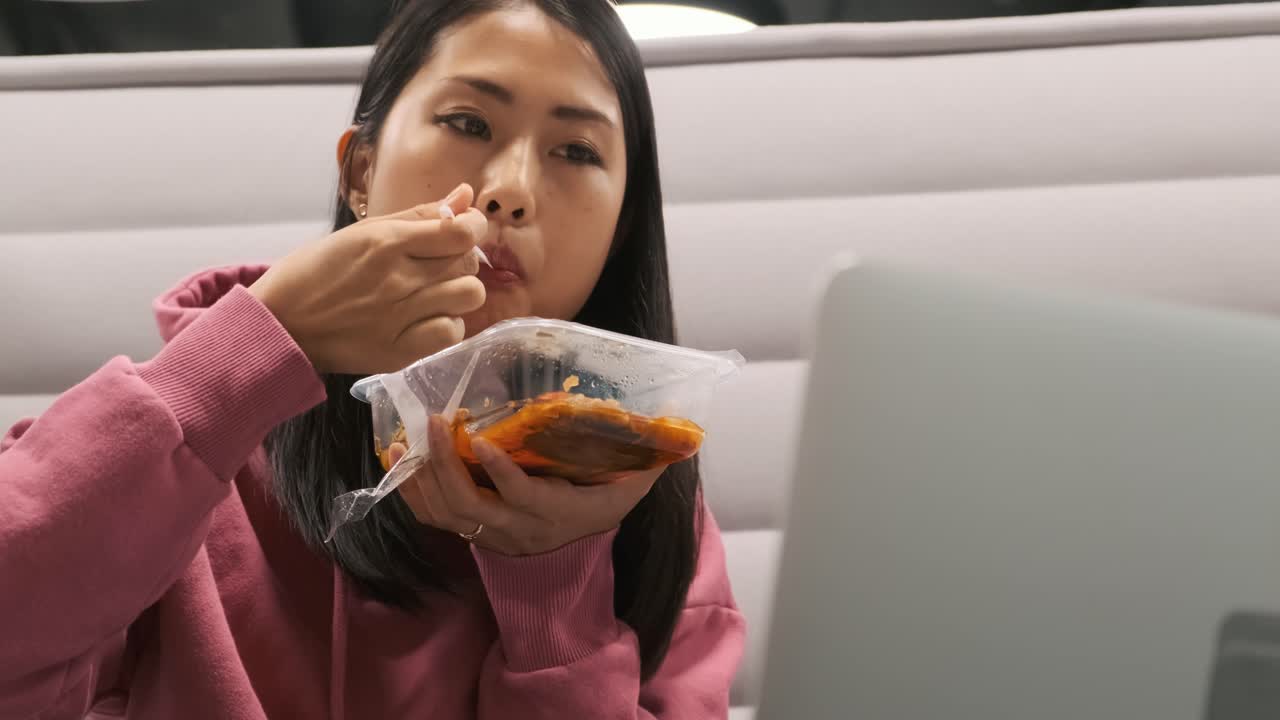 어린 여학생이 점심을 먹고 컴퓨터에서 무언가를 보고 있습니다.