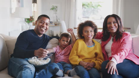 two kids and their grandparents sitting on sofa watching tv, eating popcorn and laughing, close up