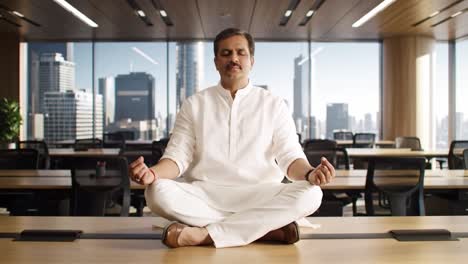 a tranquil moment of meditation: a professional man in traditional attire finds inner peace amidst a modern office environment