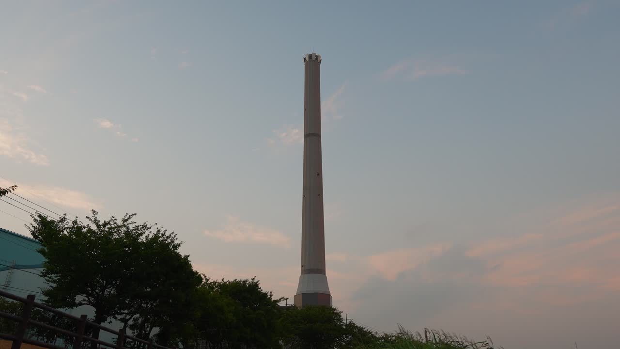 A close-up, low-angle shot of a tall, modern-looking chimney or tower against the sky at dusk