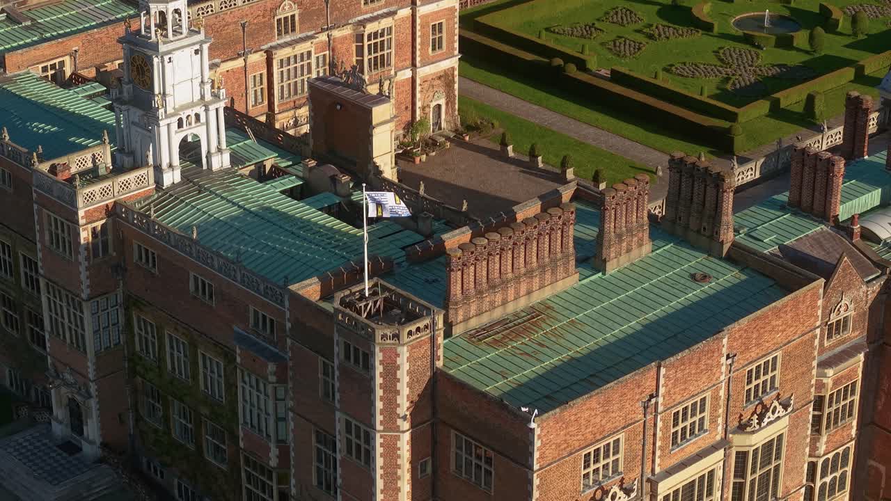 Aerial view circling Hatfield country house mansion rooftop with flag waving in the breeze