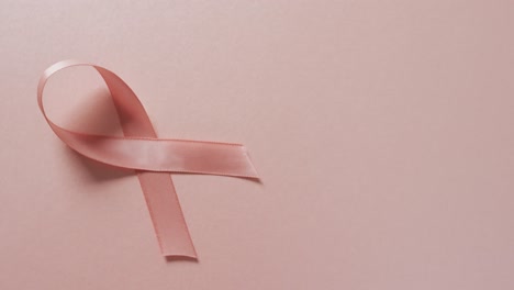 video of pink breast cancer ribbon and shadow on pale pink background